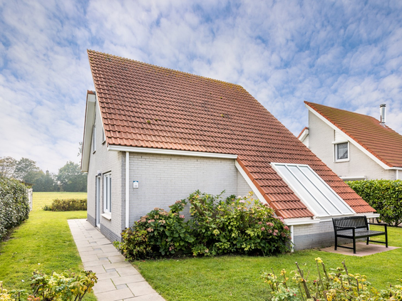 Buitenkant van een vrijstaande vakantievilla met een puntdak en een grote tuin op Vakantiepark Zeeland Village.