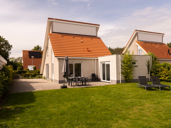 Vakantievilla op Zeeland Village met een zonnig terras en een grote, groene tuin met ligstoelen.