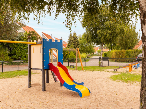 De speeltuin op Vakantiepark Zeeland Village met een kleurrijke glijbaan en een klimtoestel in het zand.