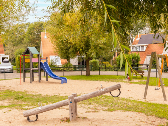 Een speeltuin op Vakantiepark Zeeland Village met een houten wipwap en een blauwe glijbaan in het zand.