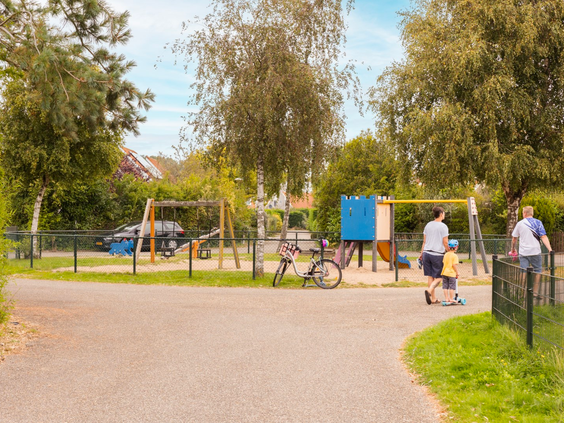 Een gezin wandelt over een pad op het groene Vakantiepark Zeeland Village richting de speeltuin.