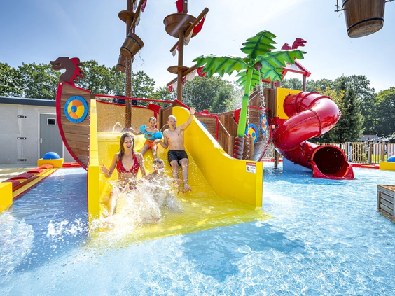 Kind glijdt van de gele glijbaan in de waterspeeltuin voor peuters