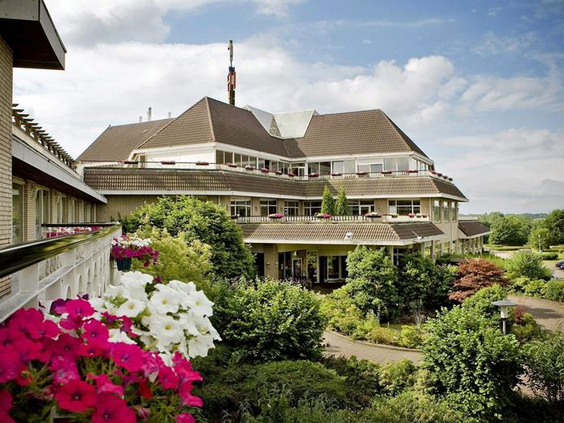 Buitenaanzicht van het kindvriendelijke Van der Valk hotel in Gladbeck, Noordrijn-Westfalen, omgeven door groene tuinen en kleurrijke bloemen.