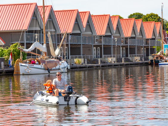 Een gezin met kinderen vaart in een rubberboot langs de waterwoningen van Waterpark Terherne op een zonnige dag.