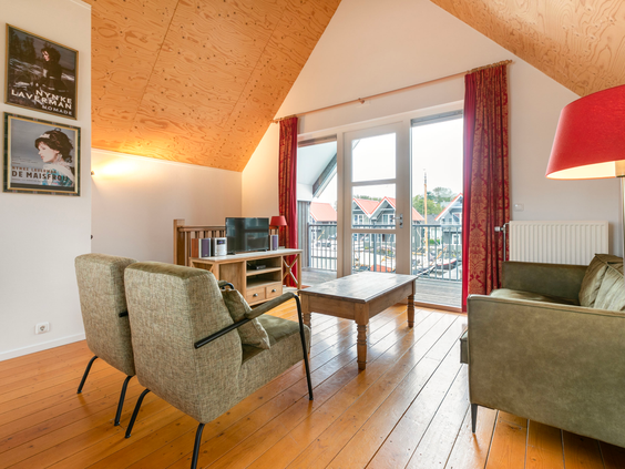 Het gezellige interieur van de woonkamer in een waterwoning, met een comfortabele zithoek en uitzicht op het water en de steigers.