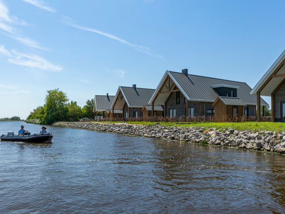 Een bootje met mensen vaart op een zonnige dag langs de moderne waterlodges van Waterpark Zwartkruis.
