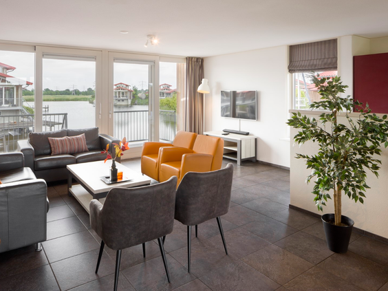 Stijlvolle woonkamer in een waterlodge op Waterpark Zwartkruis met grote ramen die direct uitzicht bieden op het water.