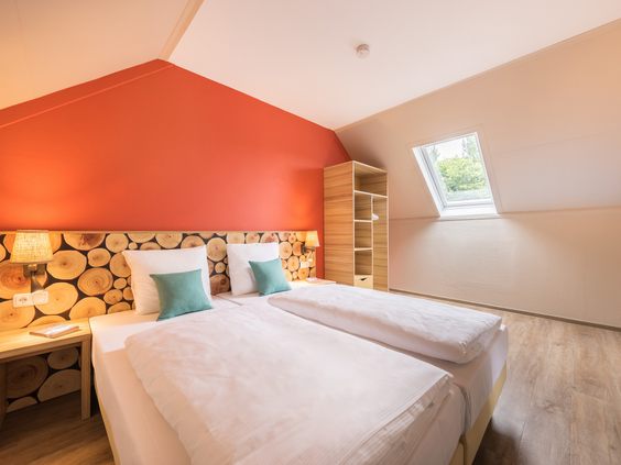 Sfeervolle slaapkamer in een vernieuwde cottage met een uniek hoofdeinde van houtblokken en een oranje accentmuur.