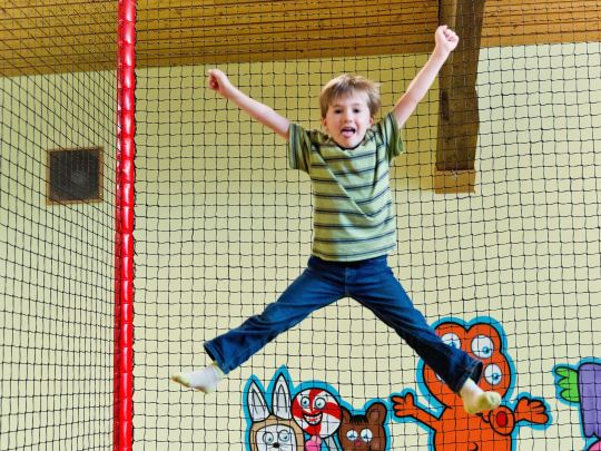 Een blije jongen springt zo hoog als hij kan op de trampoline in de binnenspeeltuin van Landal Salztal Paradies.