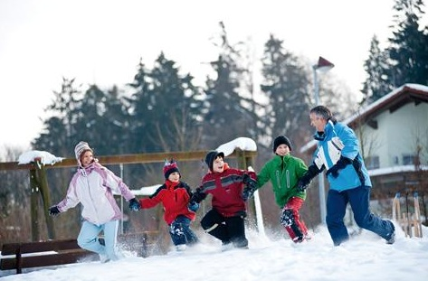 Een vrolijke familie rent hand in hand door de diepe sneeuw tijdens hun wintervakantie bij Landal Salztal Paradies in de Harz.
