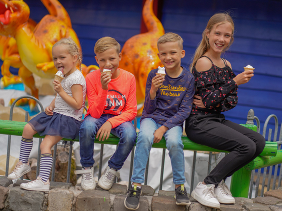 Een groep lachende kinderen zit op een muurtje en geniet van hun softijsjes in Wunderland Kalkar, waar eten en drinken inclusief is.