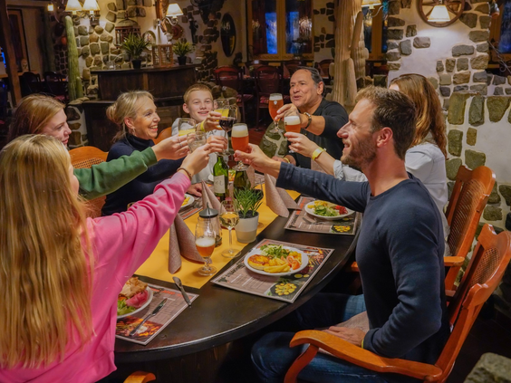 Een grote, vrolijke familie zit aan een lange tafel en proost tijdens het diner in een restaurant van Wunderland Kalkar.