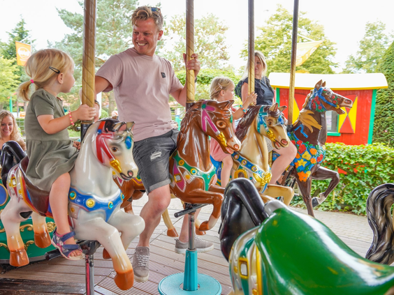 Gezin geniet van een ritje op de vrolijk gekleurde draaimolen met paarden in Wunderland Kalkar.