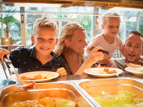 Een gezin met twee kinderen schept vrolijk eten op bij het all-inclusive buffet in het restaurant van Wunderland Kalkar.
