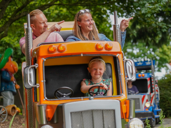 Lachend meisje achter het stuur van een oranje speelgoedtruck in een kinderattractie in Wunderland Kalkar.