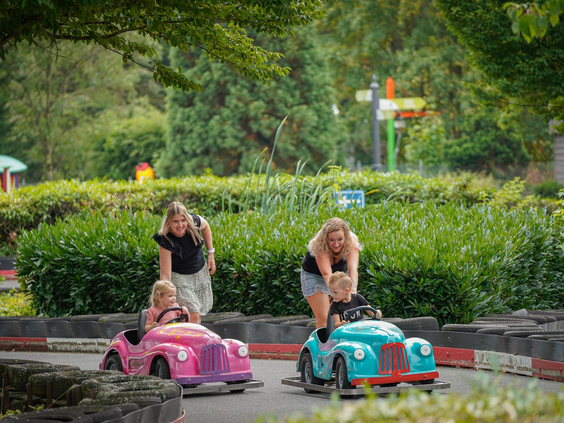 Moeders duwen hun jonge kinderen in kleurrijke speelgoedauto's op een speciaal circuit in Wunderland Kalkar.