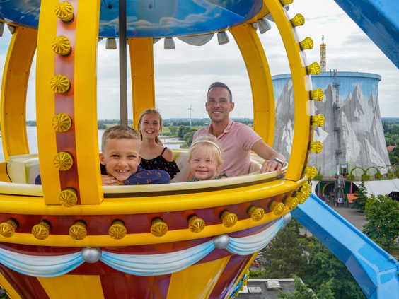 Een vrolijk gezin in een gele luchtballon-gondel van het reuzenrad in Wunderland Kalkar, met uitzicht over het park.