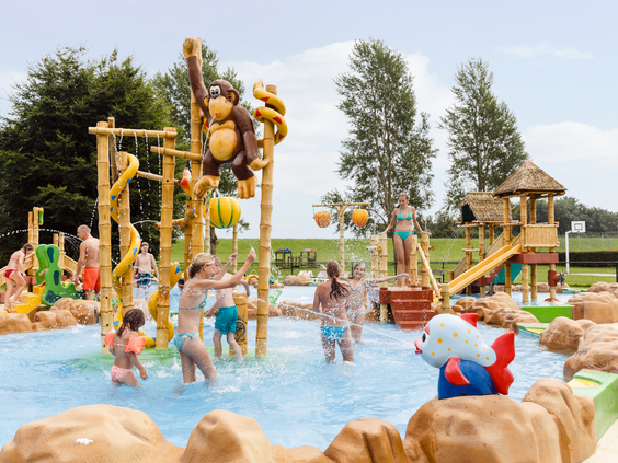 Kinderen spelen en spetteren in een vrolijke waterspeeltuin (spraypark) met jungle-thema en glijbanen in Zeewolde.