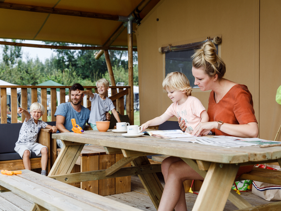 Een gezin speelt een bordspel aan de picknicktafel op de houten veranda van hun safaritent in Zeewolde.