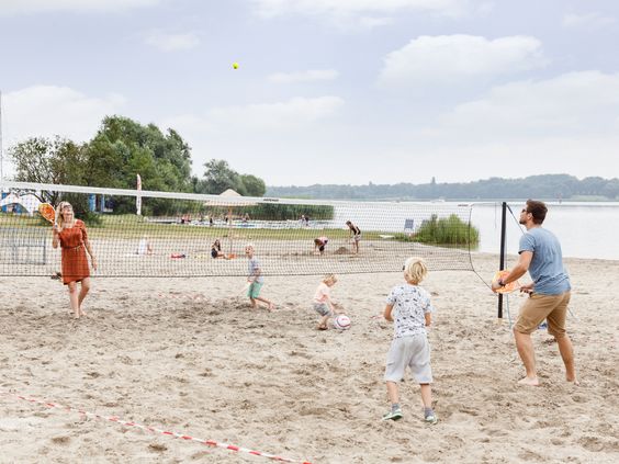 Meerdere families spelen een potje beachvolleybal op het brede zandstrand aan het water in Zeewolde.