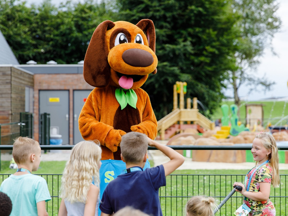 Een grote, vrolijke hond mascotte van het animatieteam geeft een high five aan de kinderen op het vakantiepark in Zeewolde.