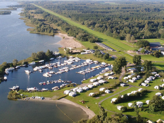 Luchtfoto van een vakantiepark in Zeewolde, prachtig gelegen aan het water met een eigen strand en jachthaven vol met bootjes.