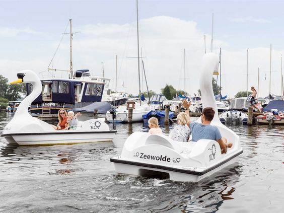 Twee gezinnen varen in witte waterfietsen in de vorm van een zwaan door de jachthaven van Zeewolde.