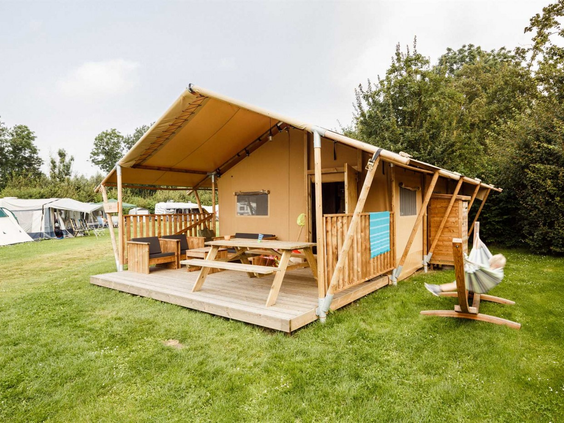 Een luxe houten safaritent (glamping) met veranda op een groen grasveld op een vakantiepark in Zeewolde, Flevoland.