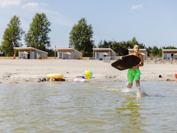 Een jongen met een bodyboard rent het water in vanaf het zandstrand op een vakantiepark in Zeewolde.