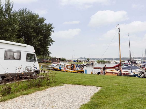 Een ruime kampeerplaats met een camper direct aan het water, met uitzicht op de jachthaven van Zeewolde, Flevoland.