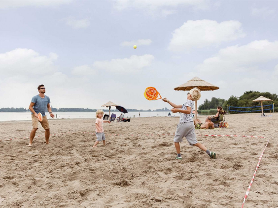 Een gezin speelt een potje beachtennis op het zandstrand aan het water in Zeewolde, Flevoland.