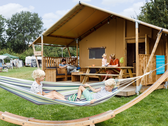 Twee jongens ontspannen in een hangmat voor hun luxe glamping safaritent op een vakantiepark in Zeewolde.