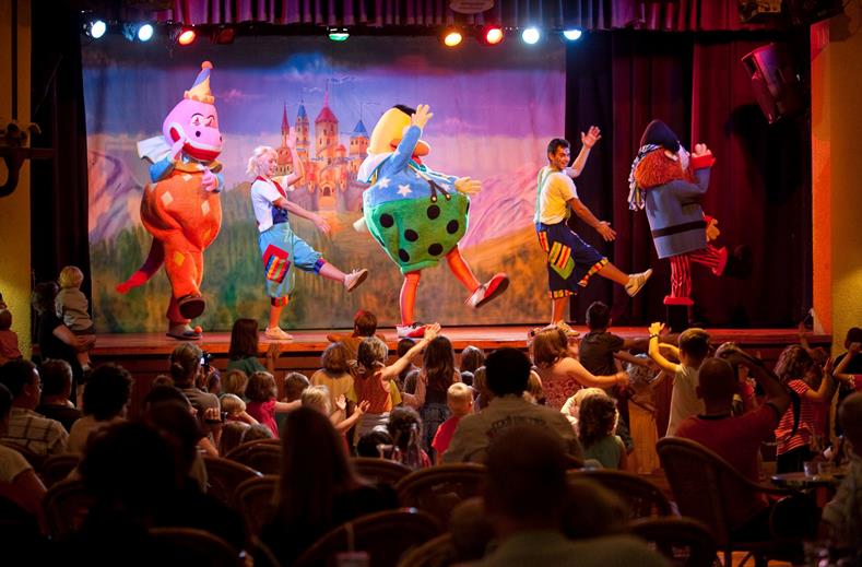 Kinderen dansen en kijken naar een vrolijke theatershow met mascottes en entertainers op het podium bij Aparthotel Royal Son Bou.
