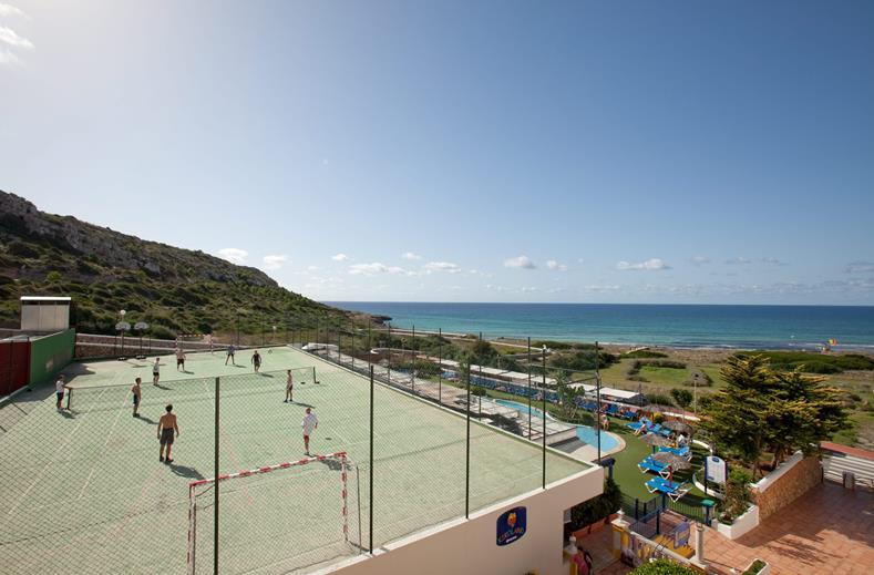 Het multifunctionele sportveld van Royal Son Bou met kinderen die voetballen, gelegen aan de kust met uitzicht op zee op Menorca.