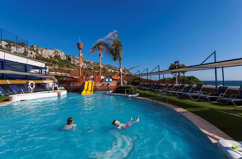 Het grote zwembad bij Aparthotel Royal Son Bou met op de achtergrond het kinderbad met piratenschip en waterglijbaan, gelegen aan de kust van Menorca.