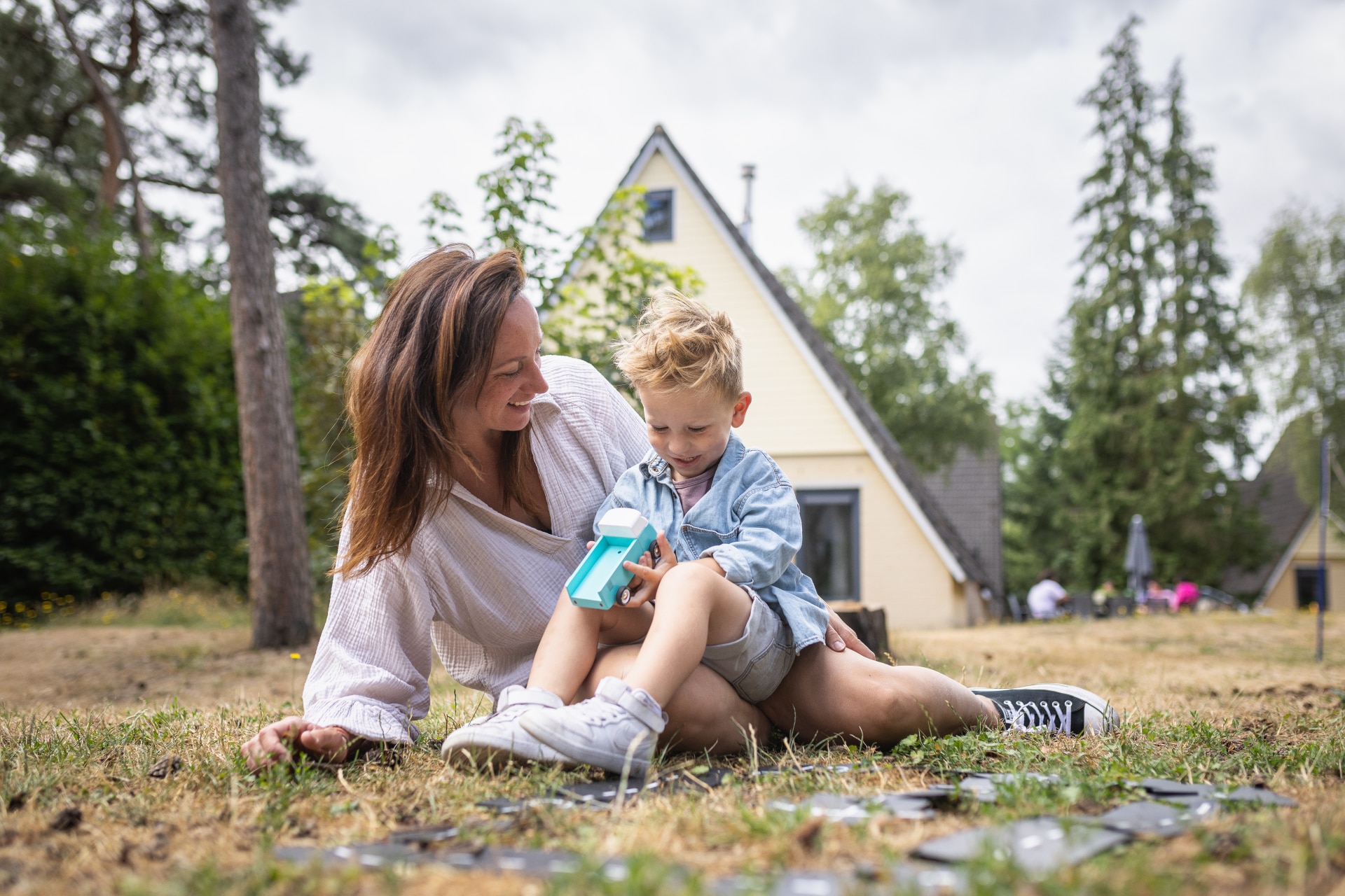 Een moeder en haar zoontje zitten op een kleed in het gras voor hun bungalow te spelen met een bellenblaas op vakantiepark De Katjeskelder.