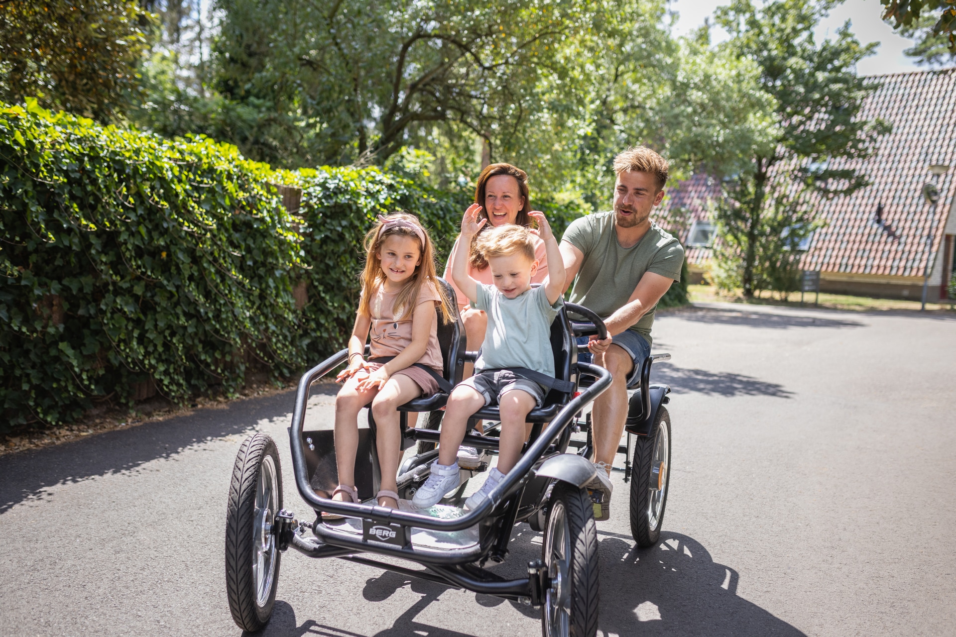 Een vrolijk gezin met twee kinderen rijdt in een grote familieskelter over een pad op vakantiepark De Katjeskelder.