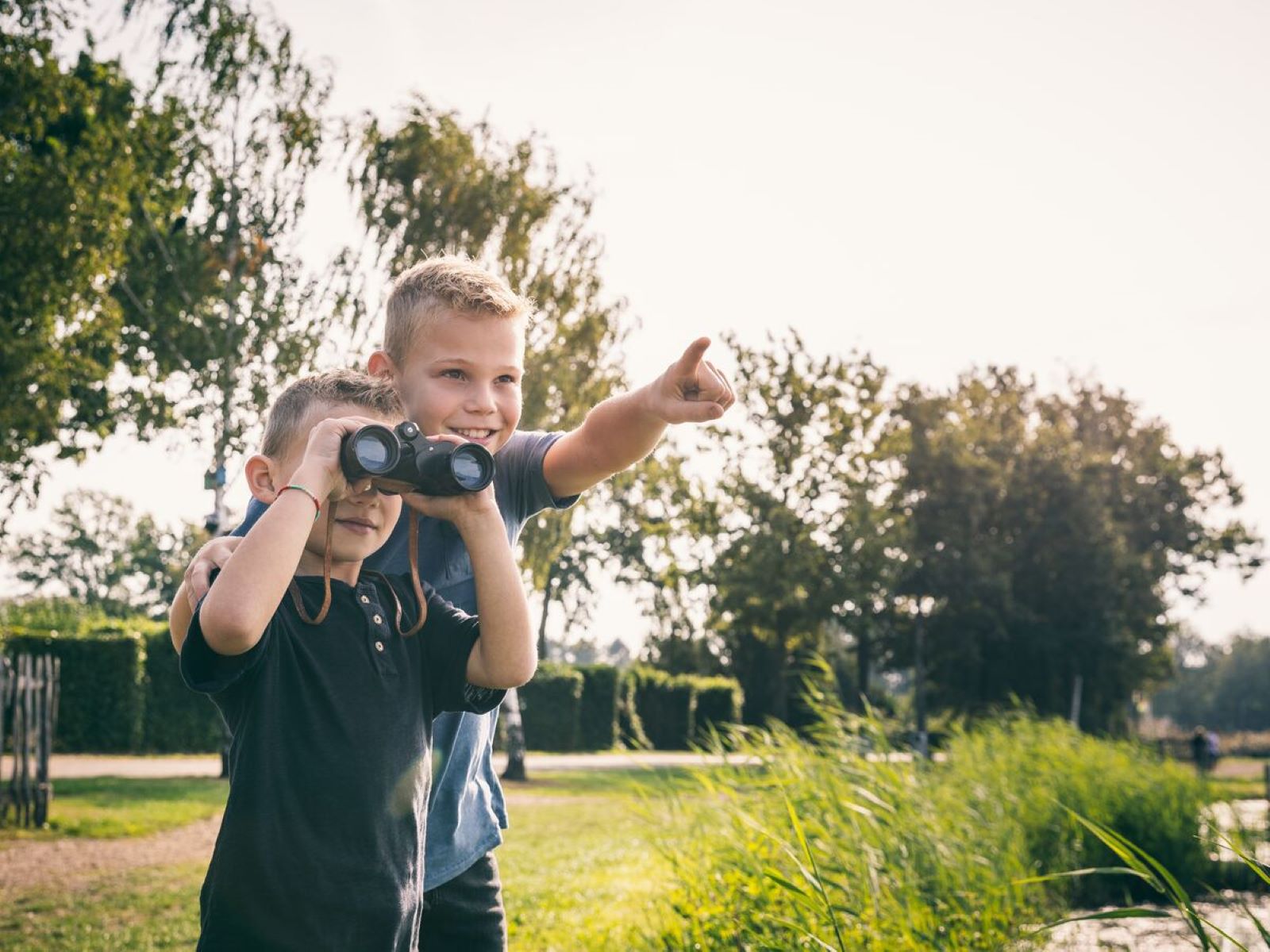 Twee jongens kijken met een verrekijker naar de natuur op het terrein van Camping de Schatberg.