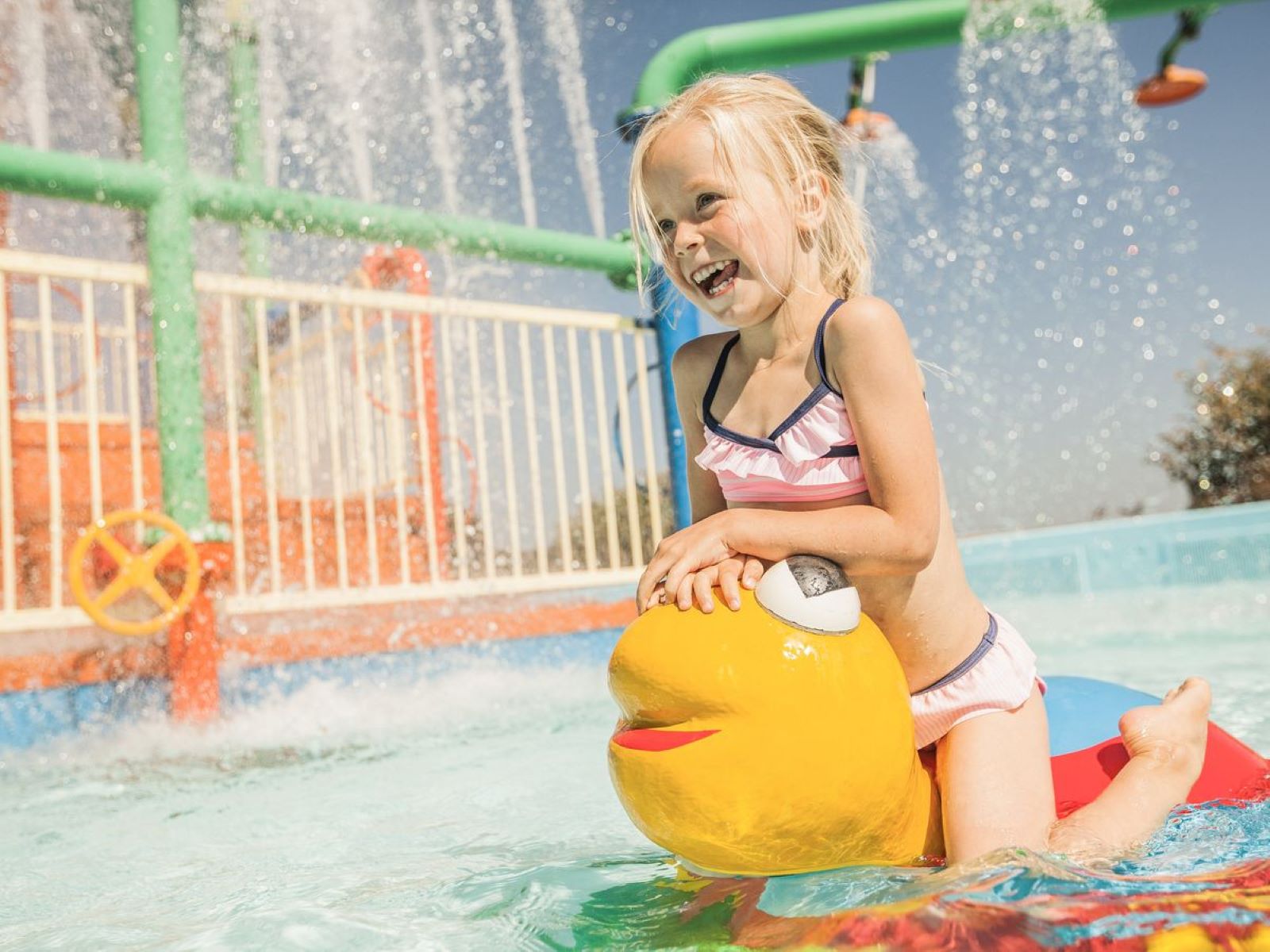 Meisje heeft plezier in het spraypark met een geel waterelement op Camping de Schatberg.