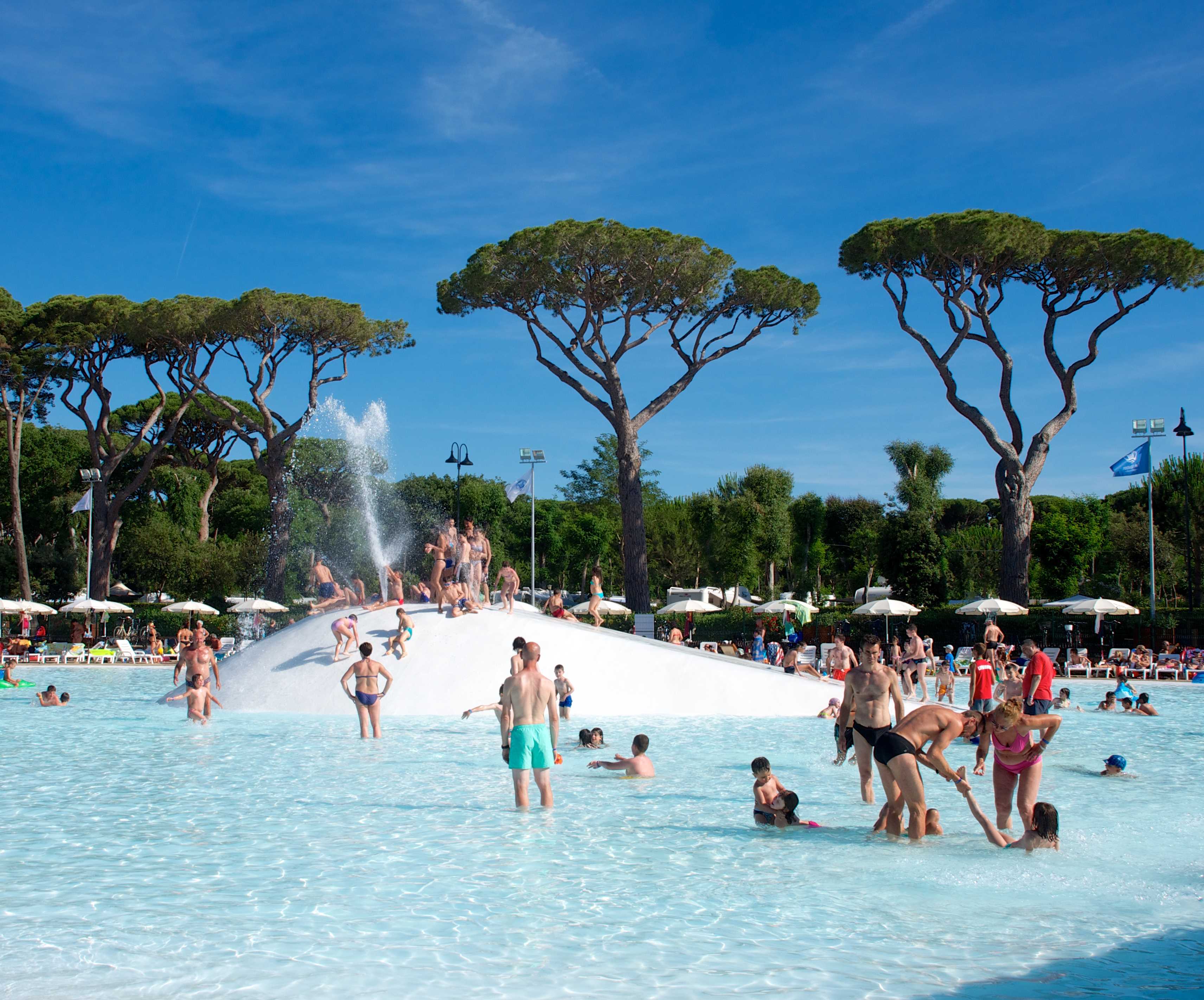 Gasten zwemmen in het kindvriendelijke lagune zwembad met zachte bodem en fonteinen, omringd door pijnbomen op camping Park Albatros in Toscane.