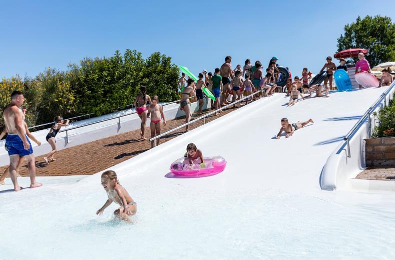 Kinderen glijden met en zonder zwembanden van de brede, zachte glijheuvel in het lagune zwembad van de kindvriendelijke camping Park Albatros.