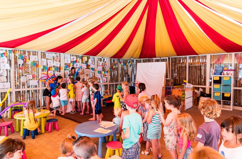 Kinderen doen mee aan creatieve activiteiten onder rood-gele circustent bij Camping Park Albatros
