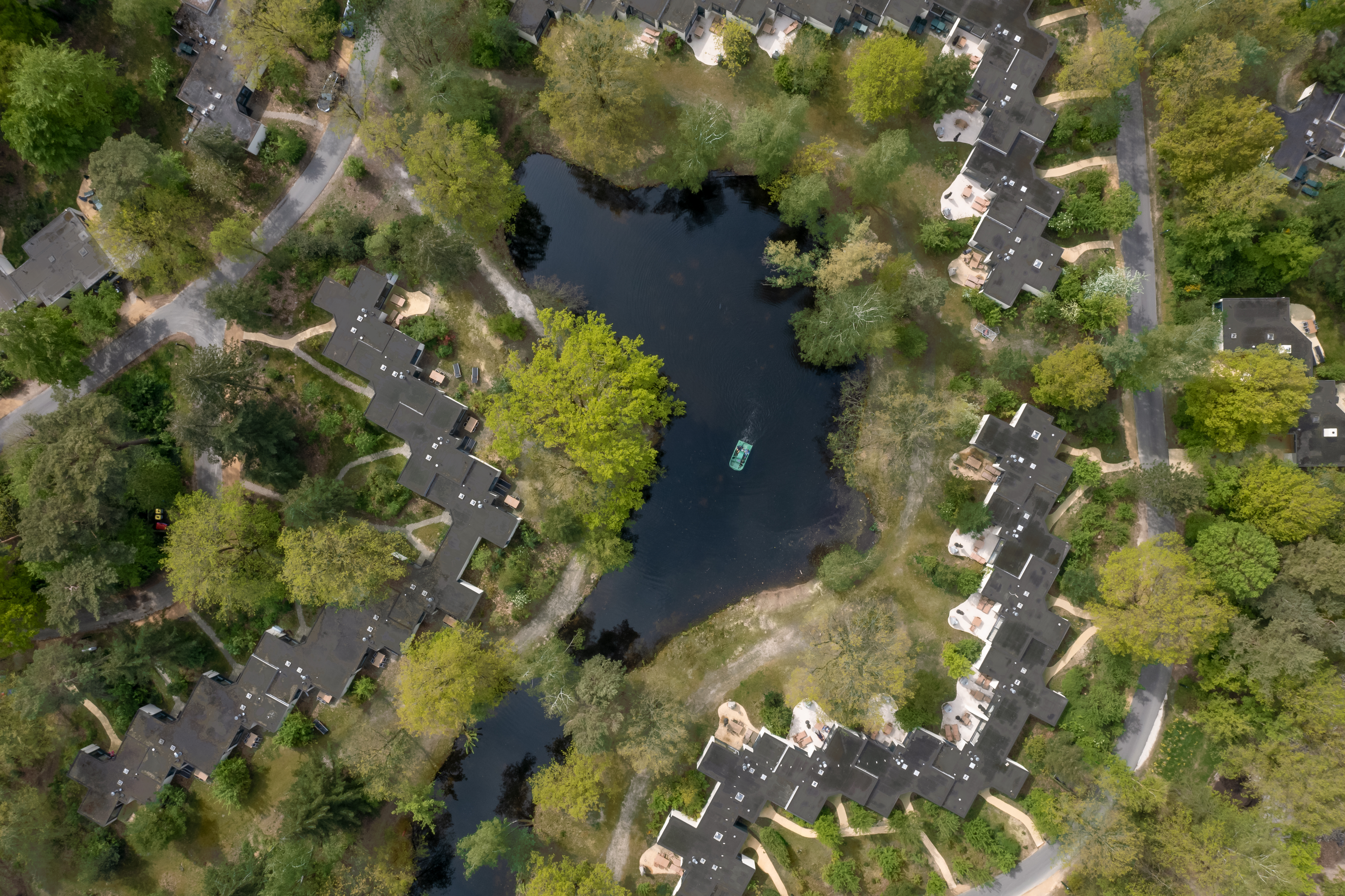 Een luchtfoto van Center Parcs Erperheide, waarop de vele cottages te zien zijn die verspreid liggen tussen de groene bomen en rondom een meer.