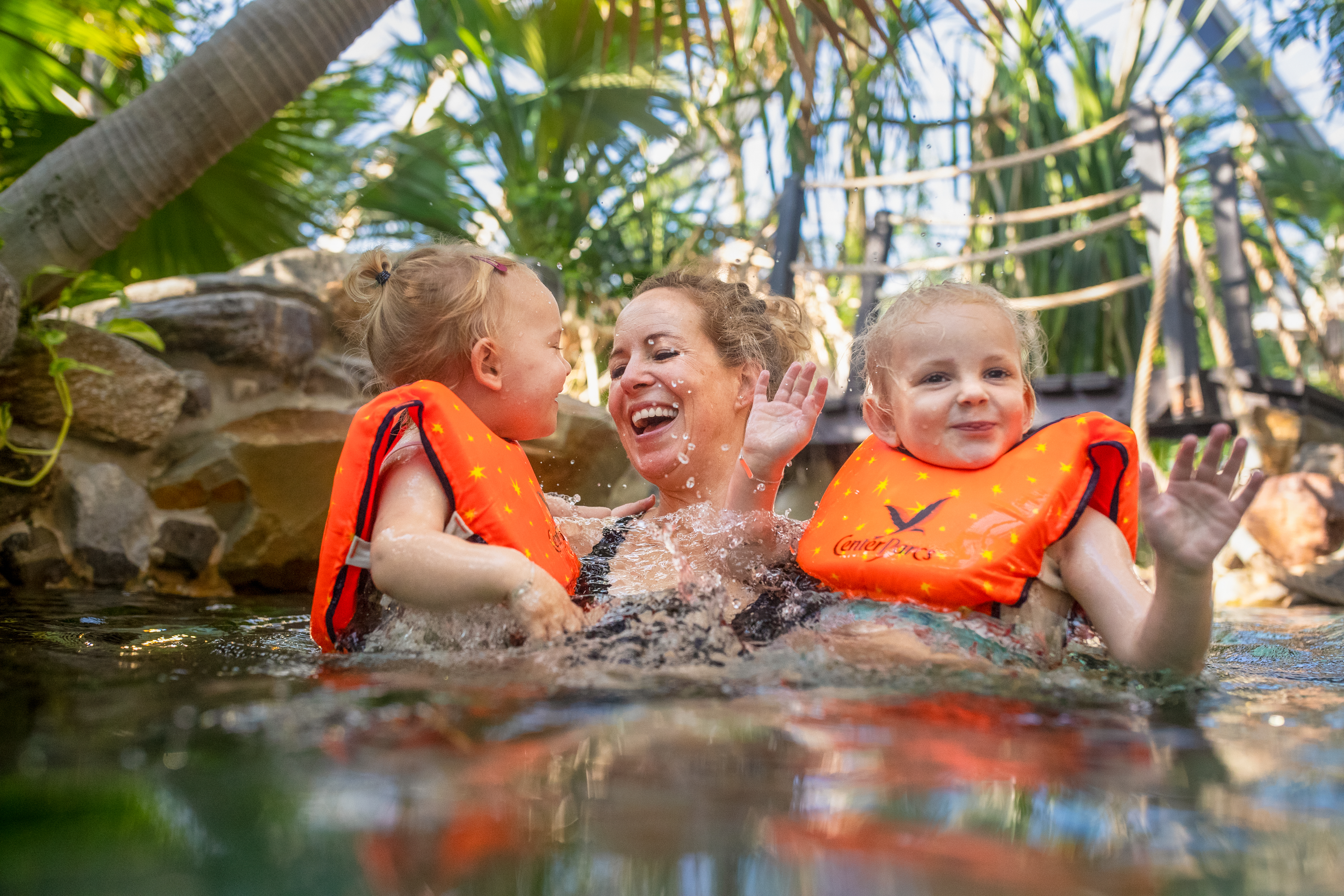 Een lachende moeder heeft plezier met haar twee jonge kinderen, die zwemvestjes dragen, in het water van de Aqua Mundo van Center Parcs Erperheide.
