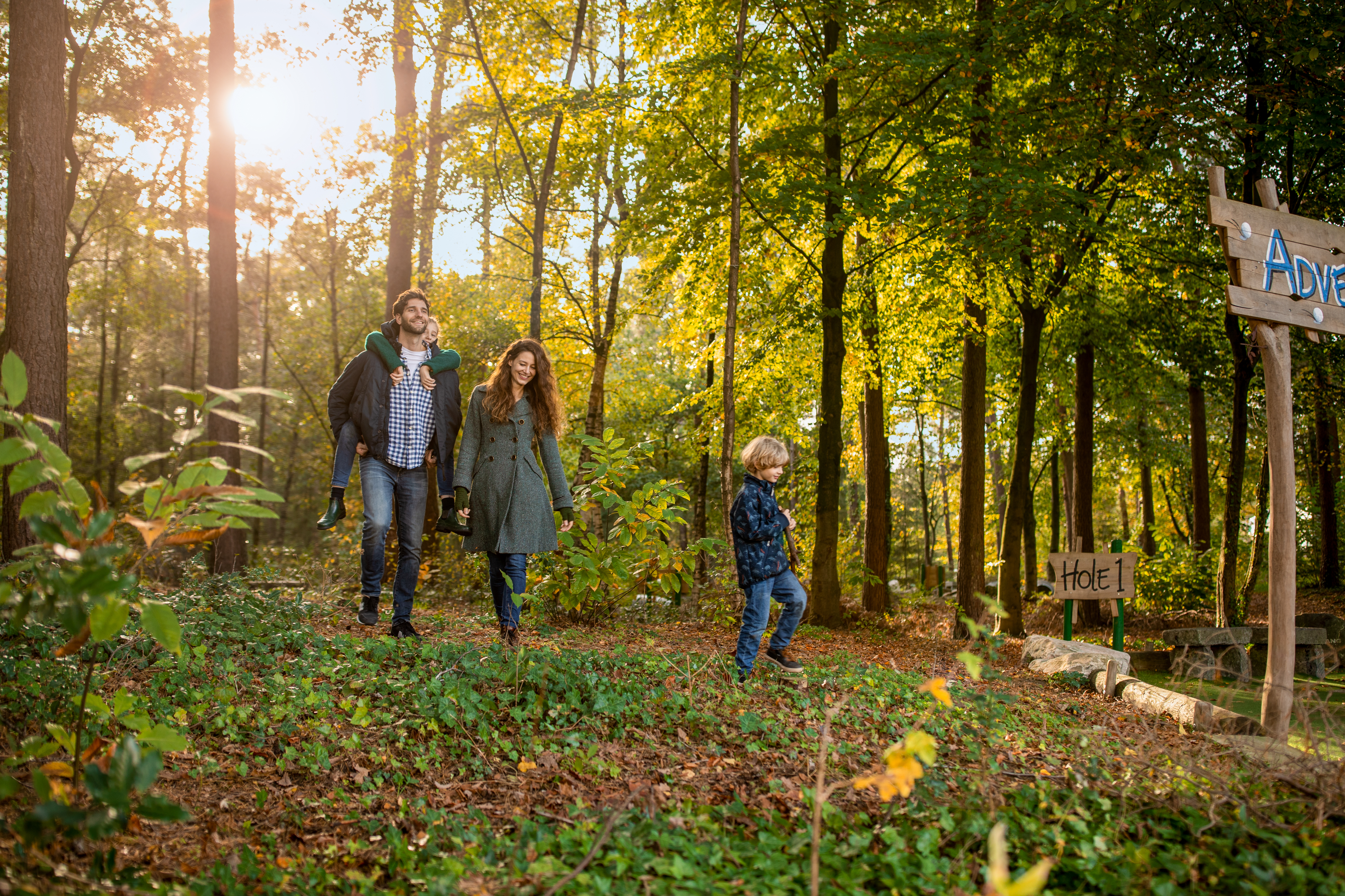 Een gezin met een jong kind maakt een wandeling over een bospad vol bladeren tijdens een zonnige dag bij Center Parcs Erperheide.
