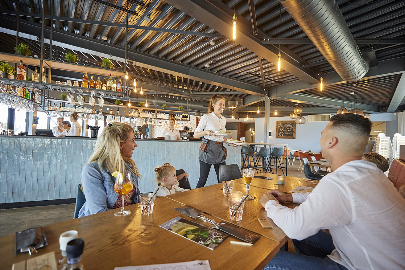Een gezin bestelt drankjes bij de serveerster in het sfeervolle familierestaurant Grillo op Recreatiepark De Leistert.