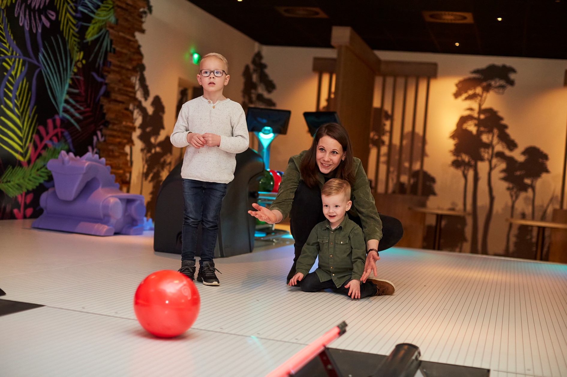 Een moeder en haar twee zonen spelen een spel met een rode bal op een interactieve speelvloer bij de bowlingbaan op Recreatiepark De Leistert.