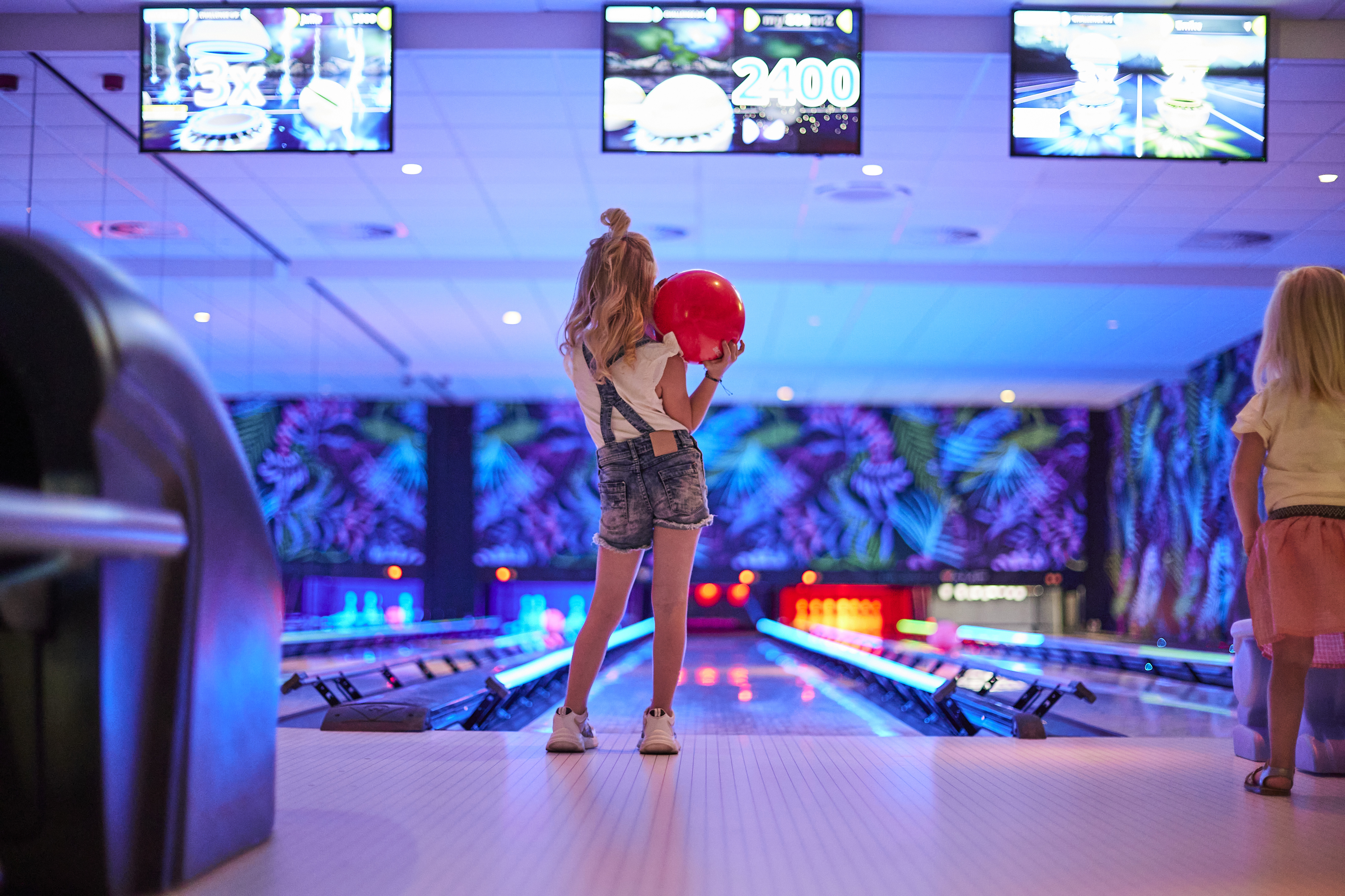Een meisje staat klaar om een rode bowlingbal te gooien op een van de kleurrijk verlichte bowlingbanen op Recreatiepark De Leistert.