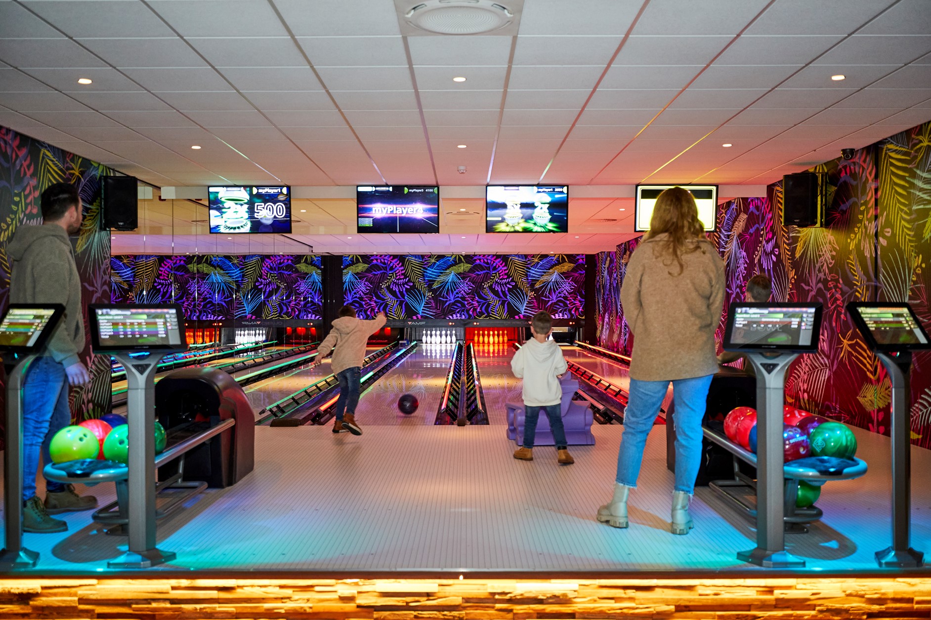Families met kinderen zijn aan het bowlen op de moderne, met discoverlichting verlichte bowlingbanen van Recreatiepark De Leistert.