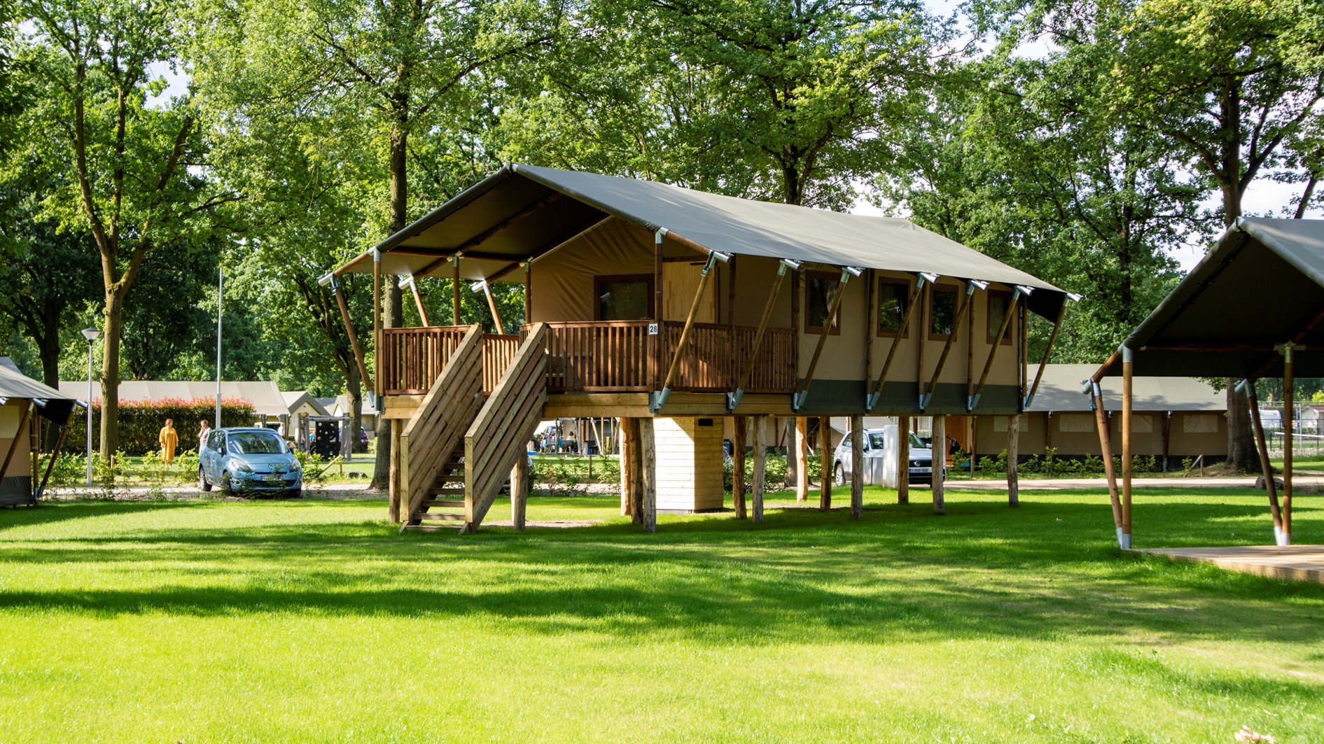 Een grote, luxe safaritent op houten palen op een grasveld op Recreatiepark De Leistert, omringd door bomen